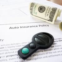 Auto insurance policy document with car key fob and rolled cash, highlighting financial aspects of car accident claims and legal representation.