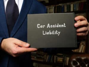 ConceptualPhotoAboutCarAccidentLiabilityWithHandwrittenPhrase | Detroit Personal Injury Attorneys Person in a suit holding a sign that reads "Car Accident Liability" in a law office setting, emphasizing legal guidance on personal injury claims related to car accidents in Michigan.